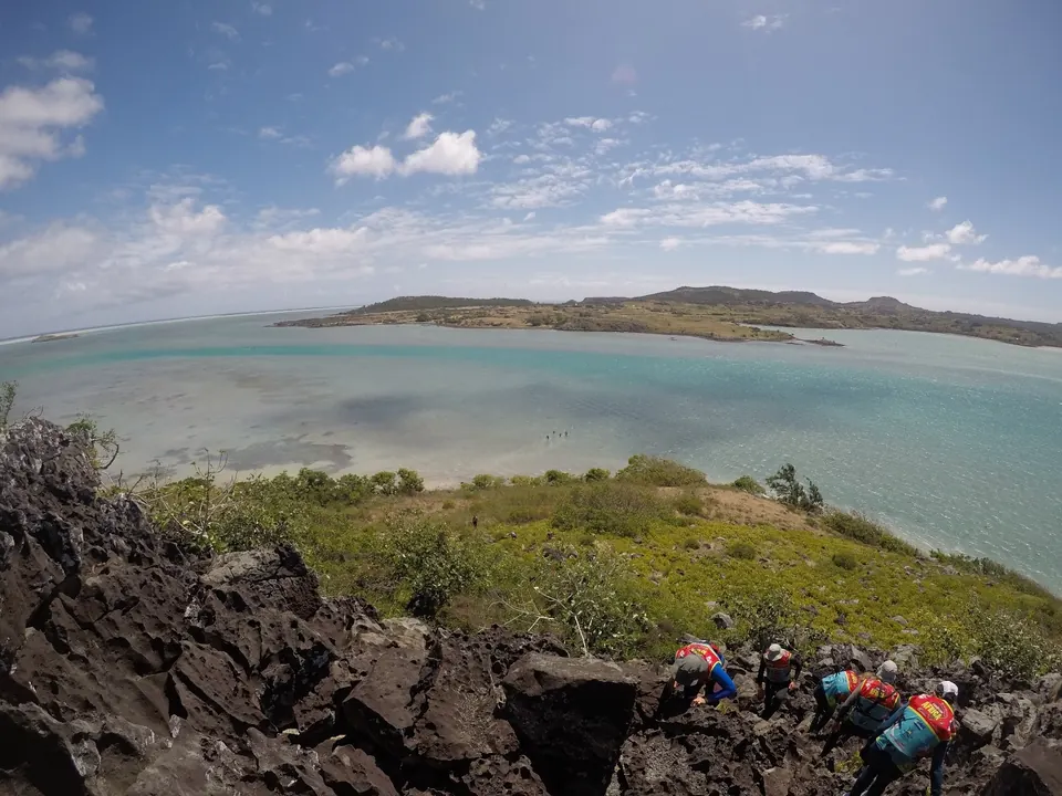 Racers scrambling over volcanic rocks above a turquoise lagoon