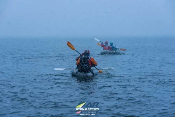 Racers paddling kayaks across a lake in the rain
