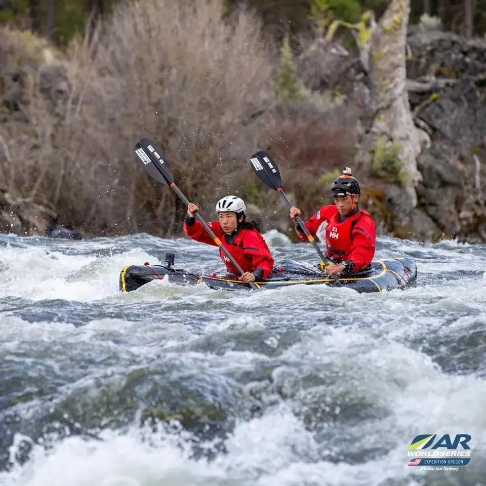 Two racers in red jackets paddling an inflatable kayak through whitewater