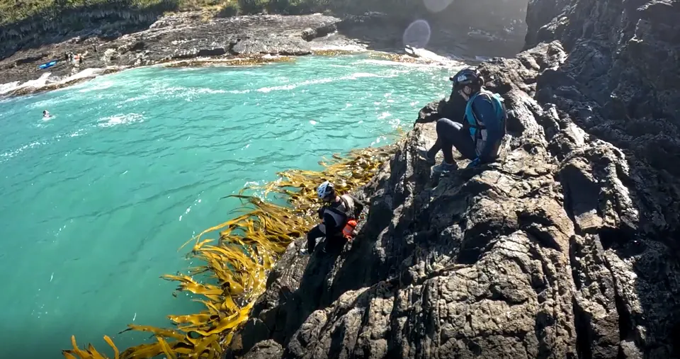 Racers climbing along a rocky coastline above turquoise water