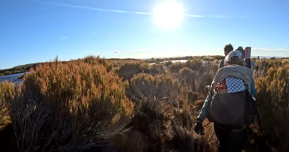 Racer with a pack trekking through scrubland under a bright sun