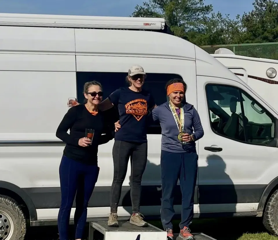 Three racers standing on a podium in front of a white van