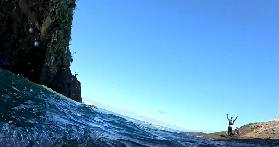 Racer standing on a distant rock at the water's edge with arms raised