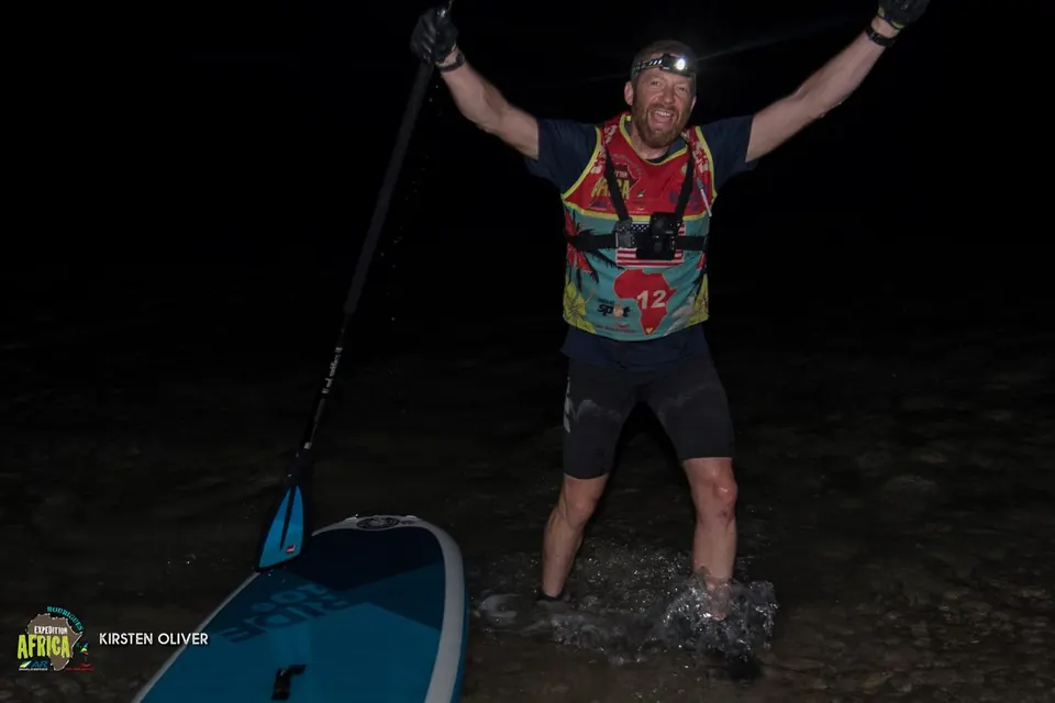Racer with a headlamp celebrating at night beside a paddleboard
