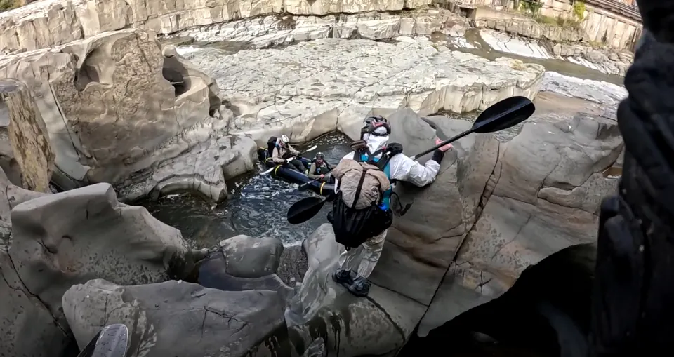 Racer carrying a paddle while moving through a rocky river gorge