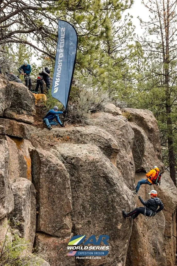 Racer rappelling down a rock face beside an Adventure Racing World Series banner