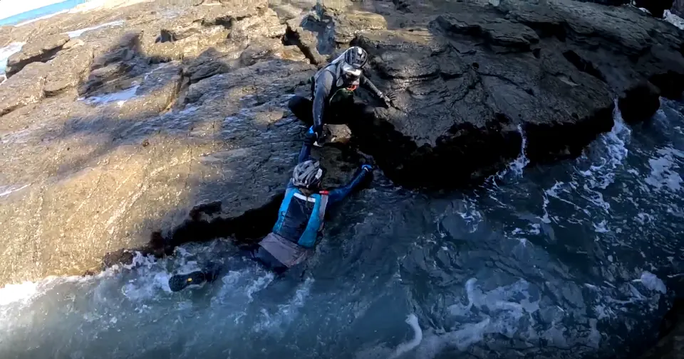 Racer in a wetsuit climbing out of the sea onto dark rocks
