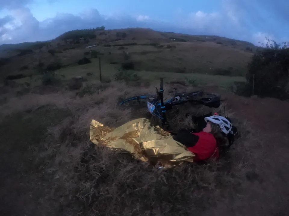 Racer resting in an emergency blanket next to bikes on a hillside