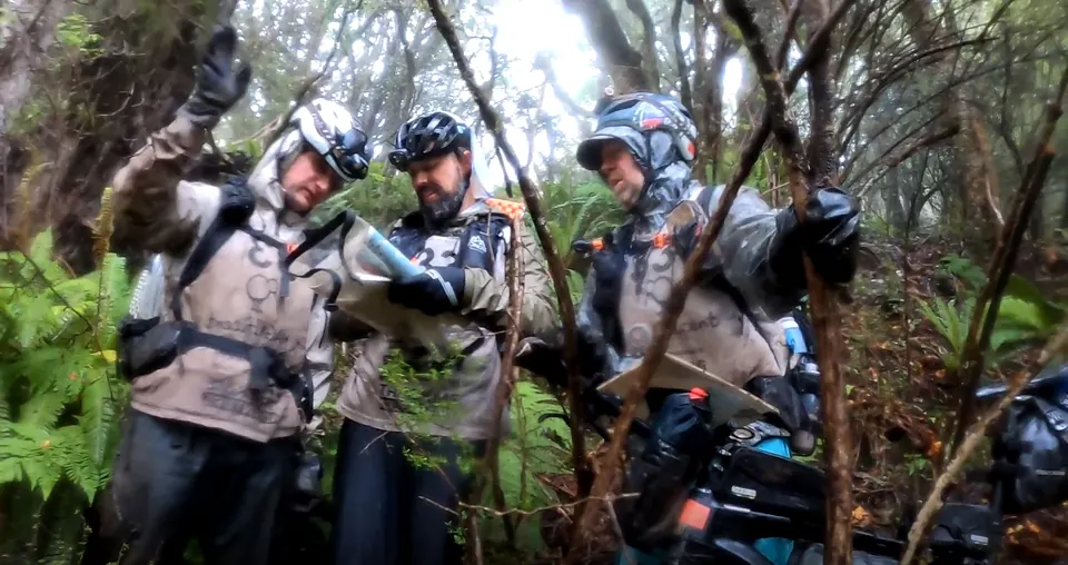 Team in rain jackets and helmets studying a map in dense bush