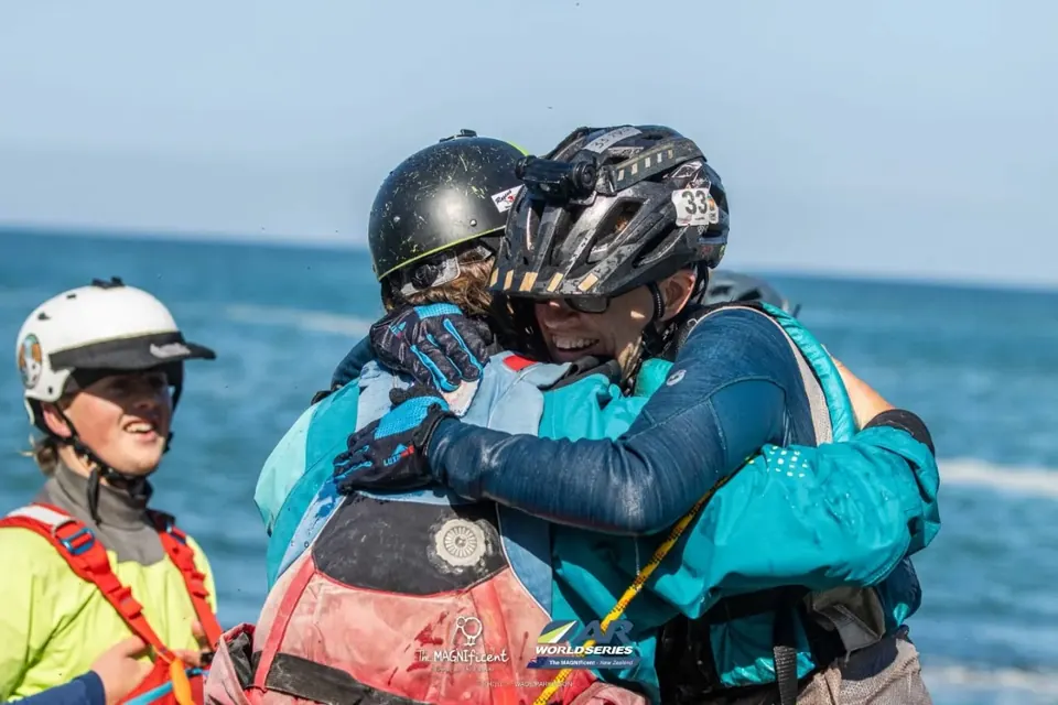 Racers in helmets and paddling gear hugging by the sea