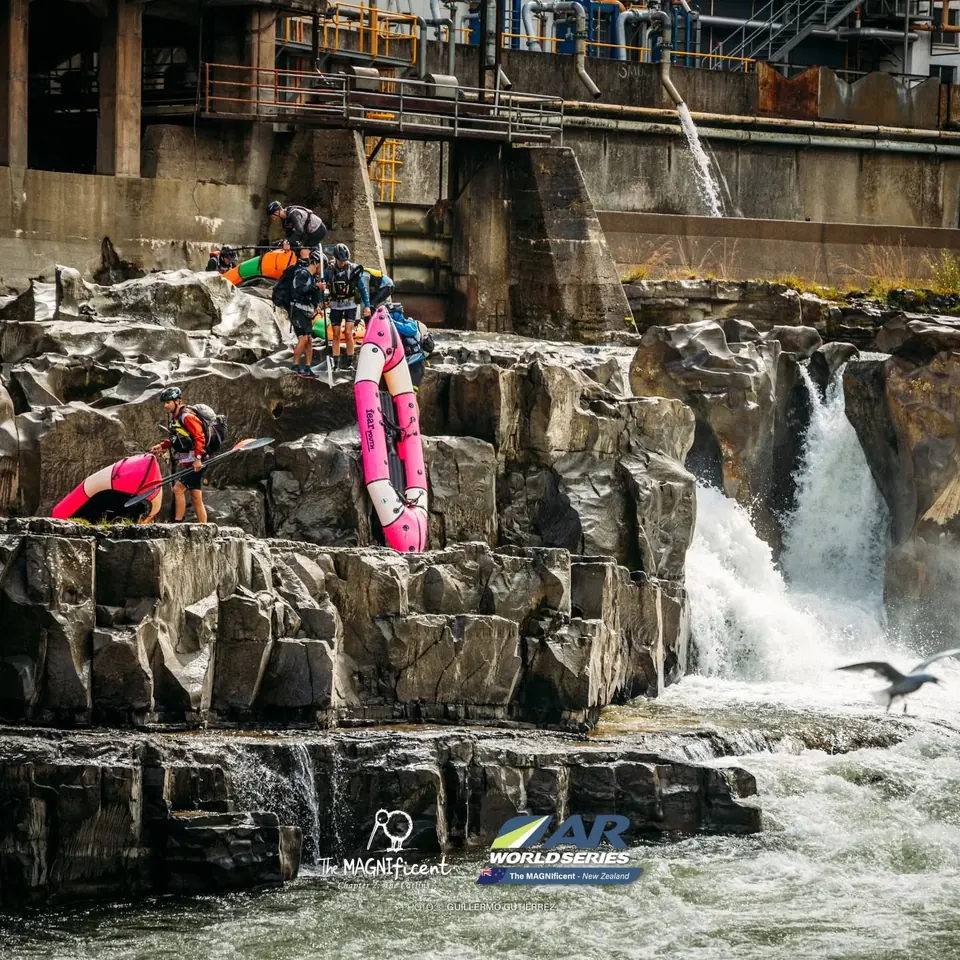 Racers climbing rocks beside a waterfall and a dam