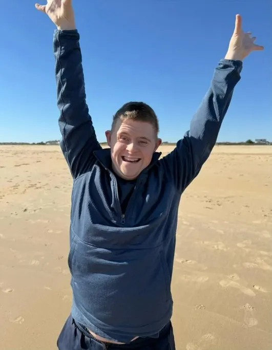 Young man on a beach smiling with both arms raised