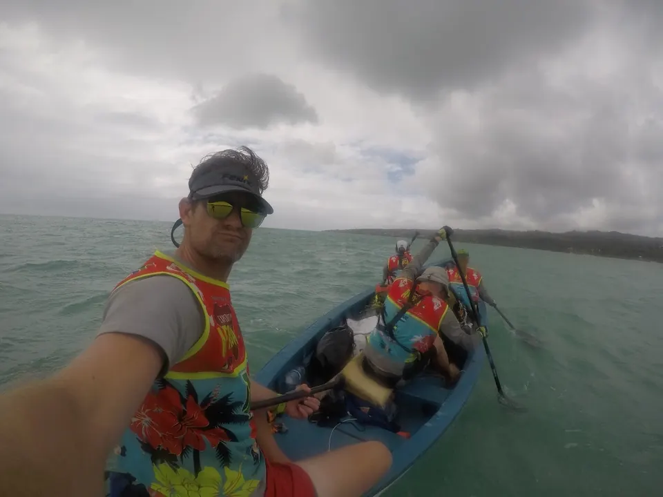 Selfie of a racer paddling a canoe with teammates on grey water