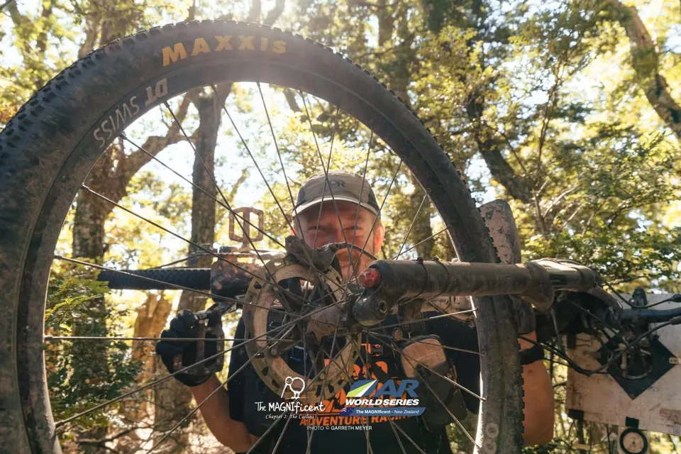 Racer holding up a muddy mountain bike with a broken drivetrain