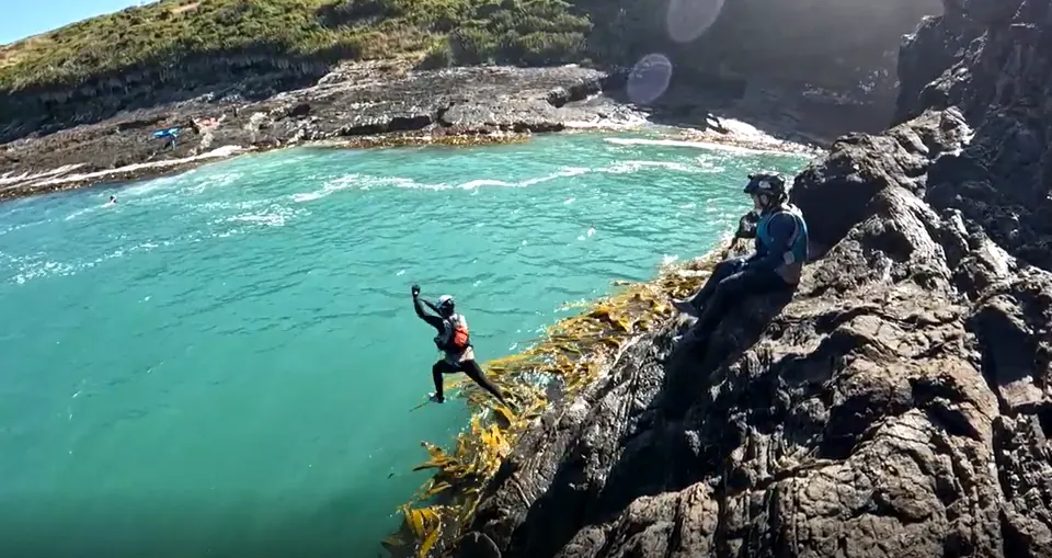 Racer jumping from a rocky coastline into turquoise water