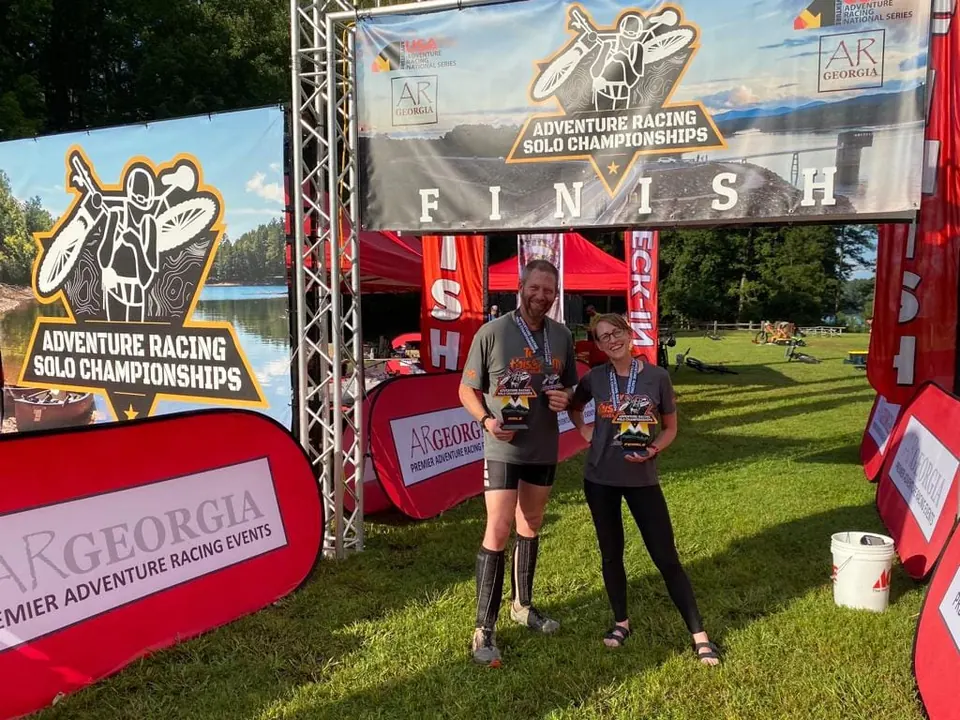 Two racers holding awards in front of a race finish arch